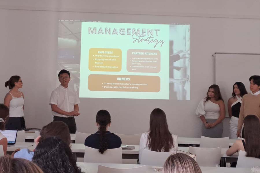 5 alumnos presentando al frente de un salón de clases. 