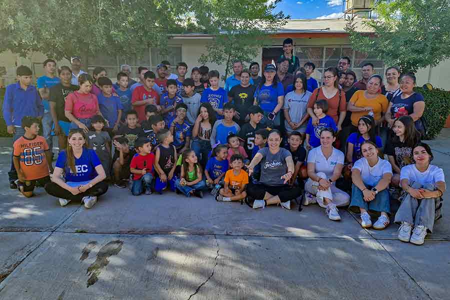 Grupo de estudiantes del Tec de Monterrey campus Chihuahua, junto a niños y familias en una actividad comunitaria al aire libre.