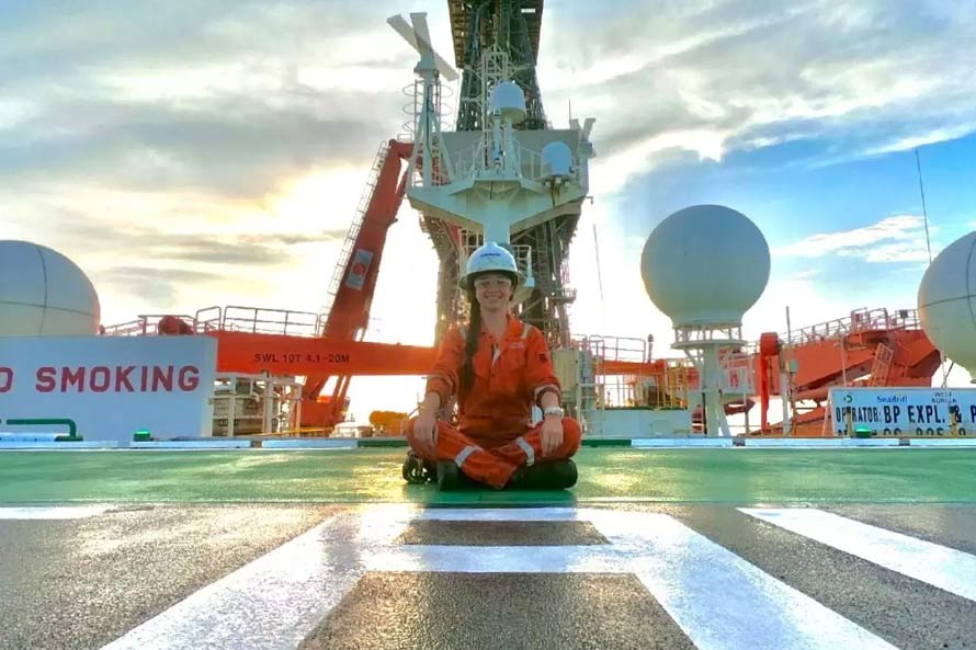 Ashly Hinojos sentada en una plataforma petrolera, sonriendo al atardecer.