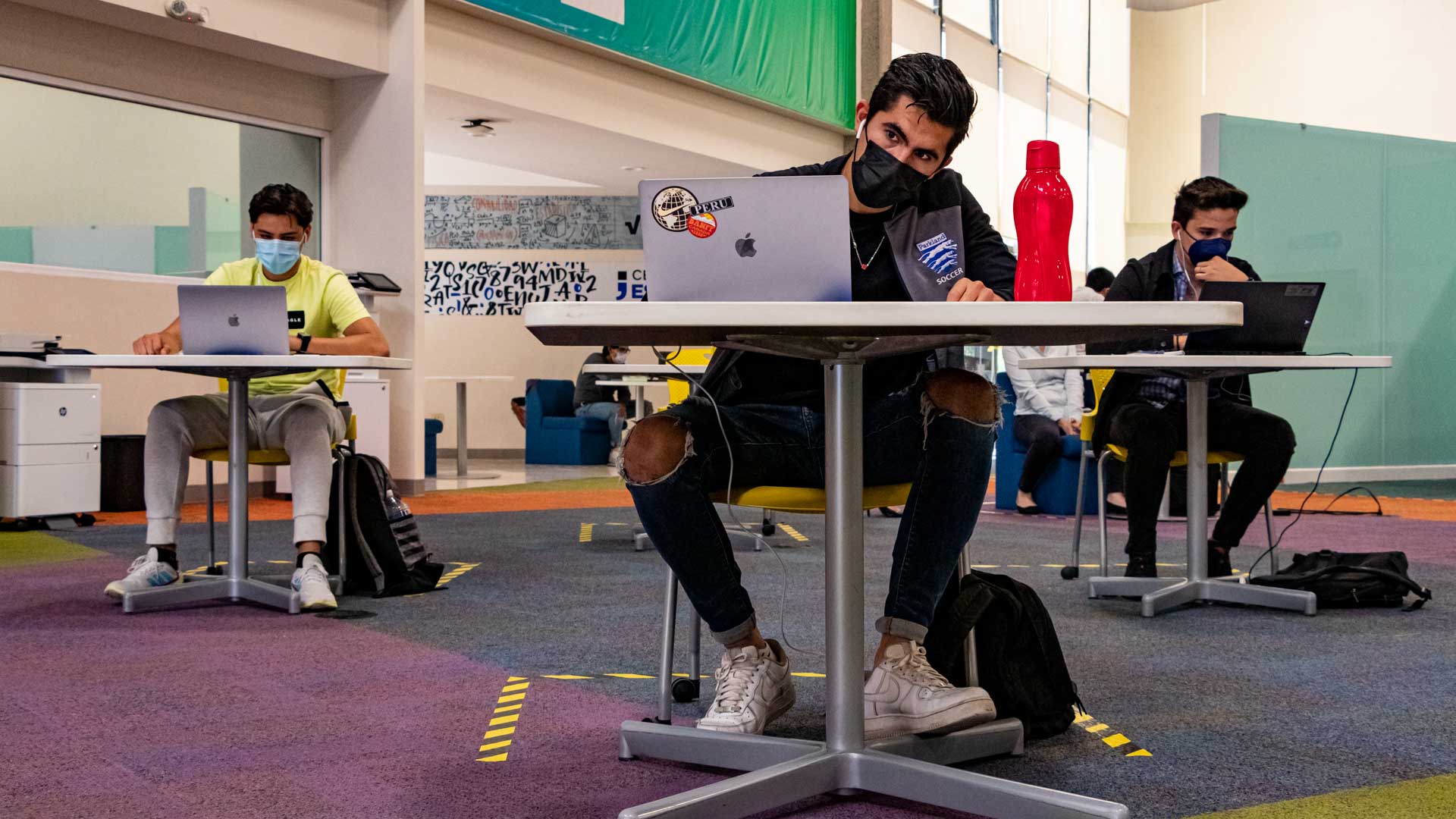 Alumnos tomando clases en el área de biblioteca, manteniendo distancia entre ellos para comprometer la salud de la comunidad.