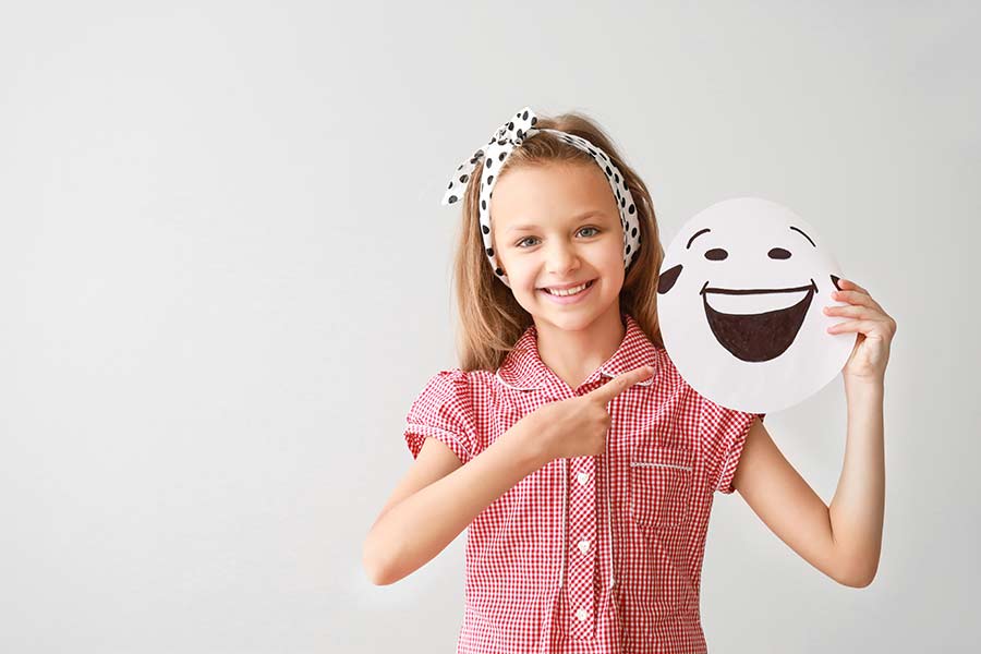 Niña sosteniendo un dibujo de una carita feliz y emocionada