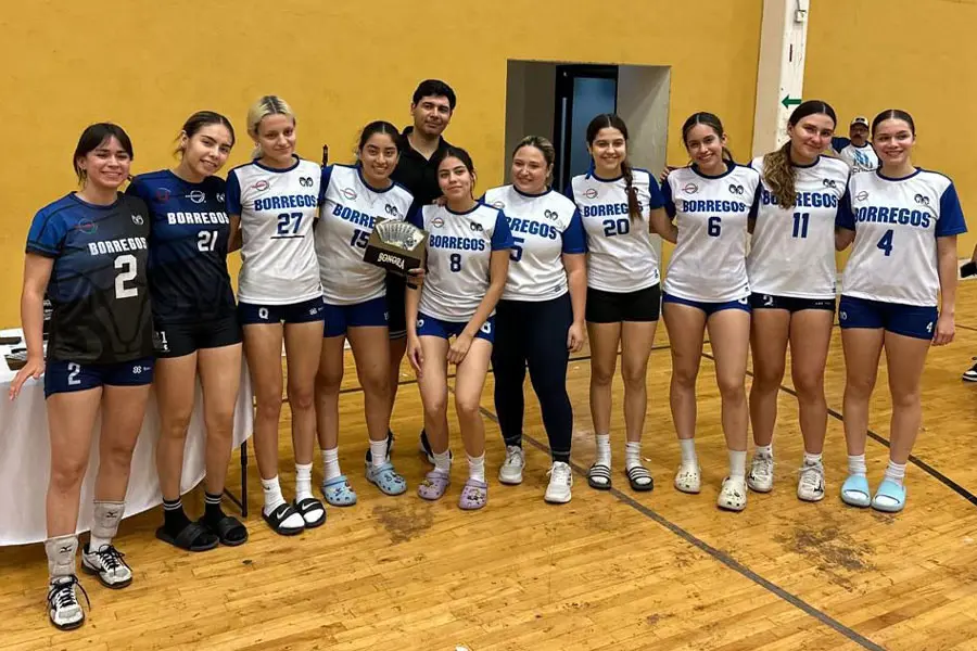 Equipo de voleibol femenil posando en grupo. Una jugadora del centro sostiene un trofeo. 