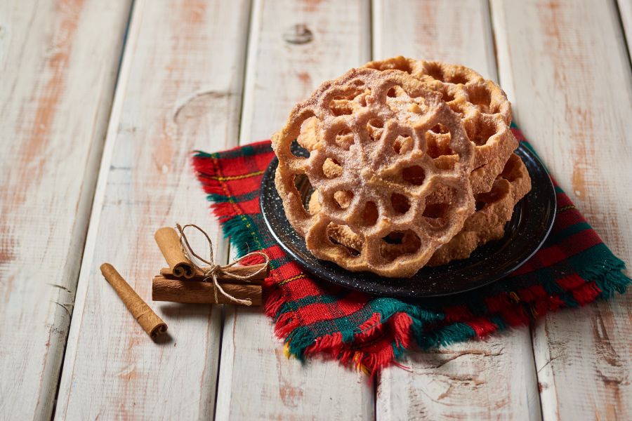 Buñuelos de viento espolvoreados con azúcar servidos en un plato sobre mantel navideño, un postre tradicional de las fiestas en México.