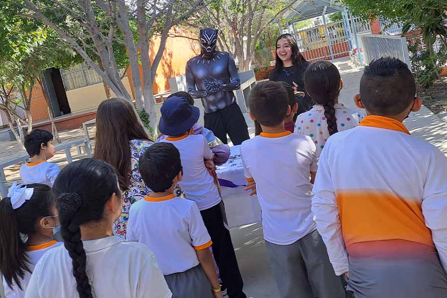 Grupo de niños frente a una joven universitaria y un joven disfrazado de Pantera Negra.