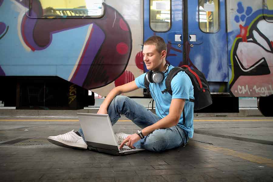 Joven escribiendo con computadora en una estación de metro