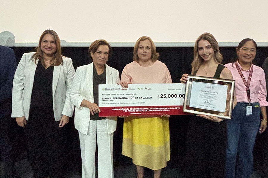 Un grupo de cuatro mujeres posa juntas, las 2 del centro sostienen un cheque gigante y la joven del extremo derecho sostiene un reconocimiento enmarcado por ganar un concurso.