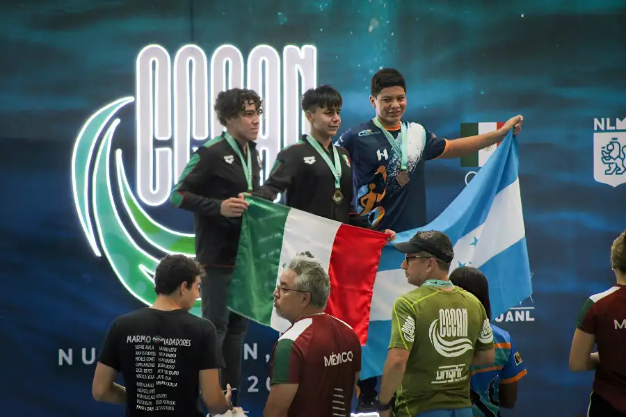 Diego Lizardi, estudiante de PrepaTec y nadador hidalguense, en el podio con la medalla de oro en el CCCAN 2024, sosteniendo la bandera de México junto a otros medallistas.