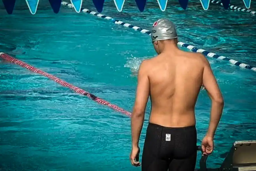 Diego Lizardi, nadador hidalguense y estudiante de PrepaTec, se prepara junto a la piscina antes de una competencia de natación, vistiendo gorra plateada y traje de competición.