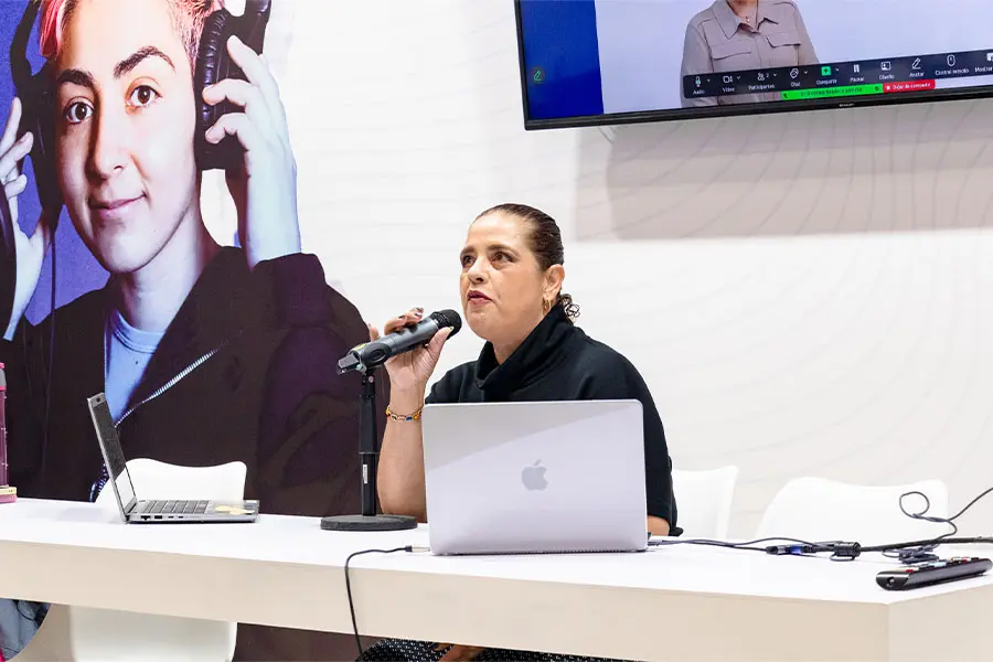 Muejer sentada en un escritorio hablando y sosteniendo un micr&oacute;fono.