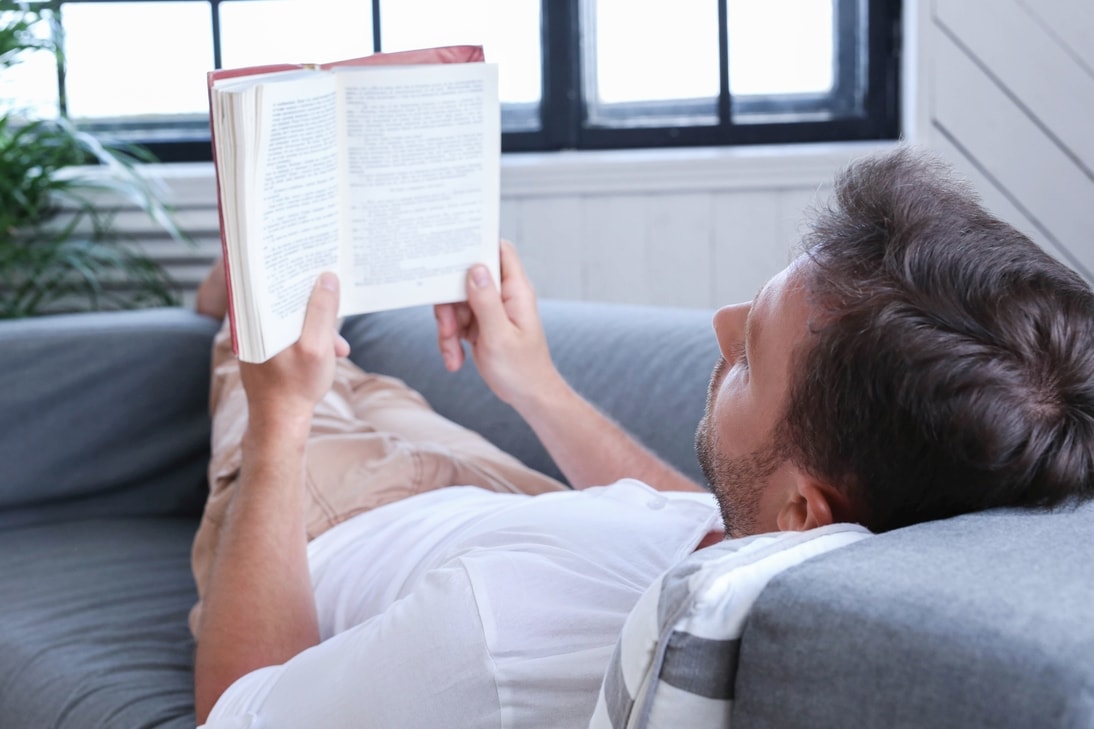 hombre acostado en sillon leyendo un libro