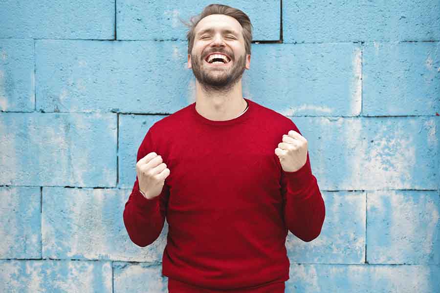 humbre con sudadera roja, con las manos al  nivel del pecho, puños cerrados y sonriendo