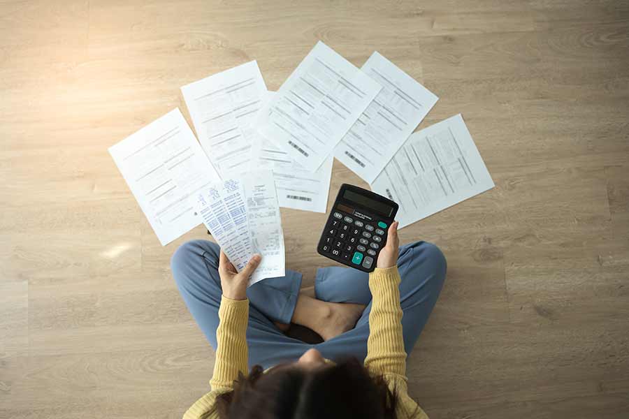 Mujer joven sentada en el piso, haciendo cuentas de sus gastos con una calculadora