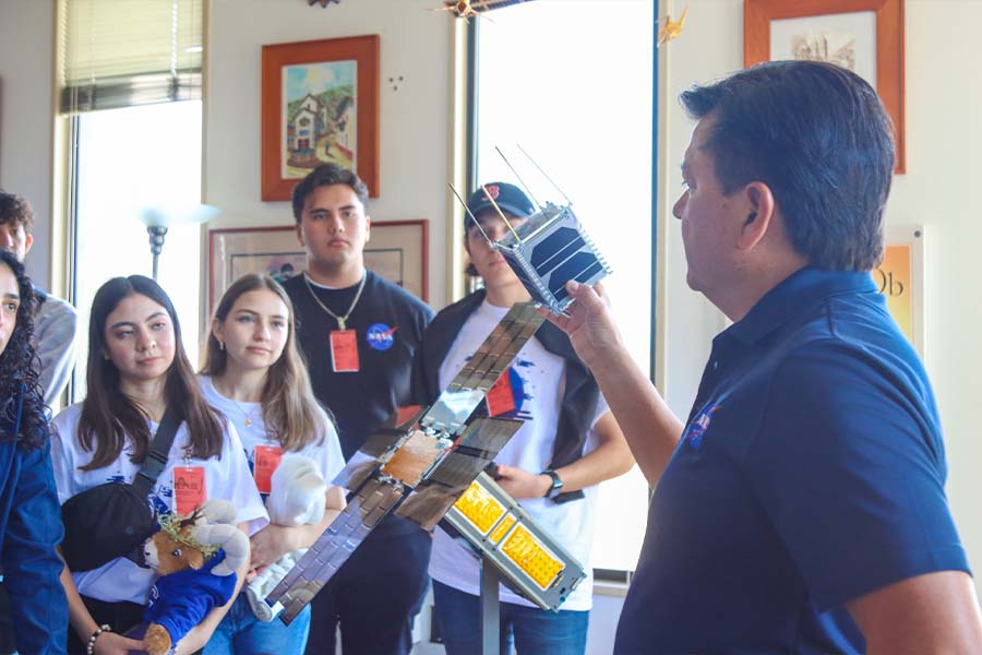 Estudiantes del Tec Sonora conversan con un investigador de la NASA en su oficina mientras el les muestra un prototipo de microsatélite.