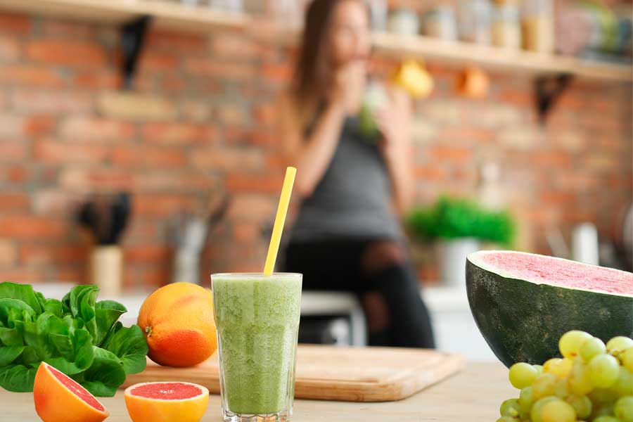 Jugo de frutas en una cocina con mujer joven de fondo