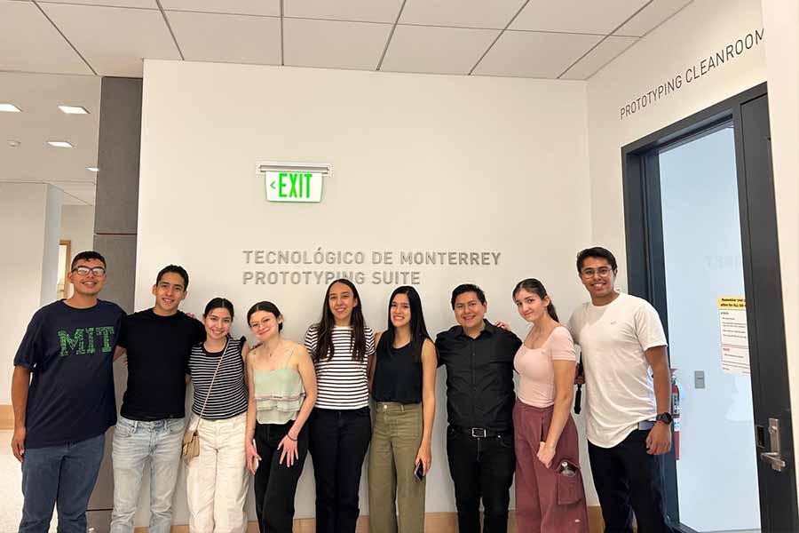 Grupo de 9 personas posando juntos frente a la entrada a un laboratorio, donde en la pared se ve un letrero que dice "Tecnol&oacute;gico de Monterrey Prototyping Suite".