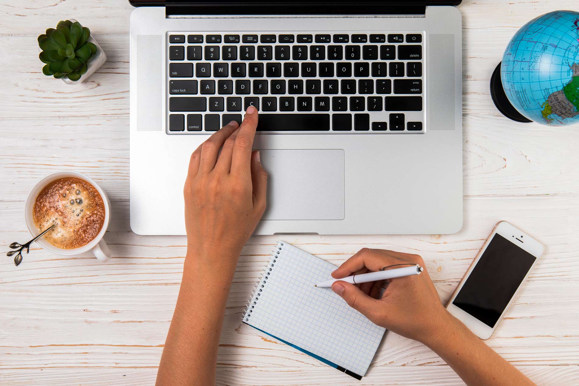 Manos escribiendo en laptop con una libre de notas