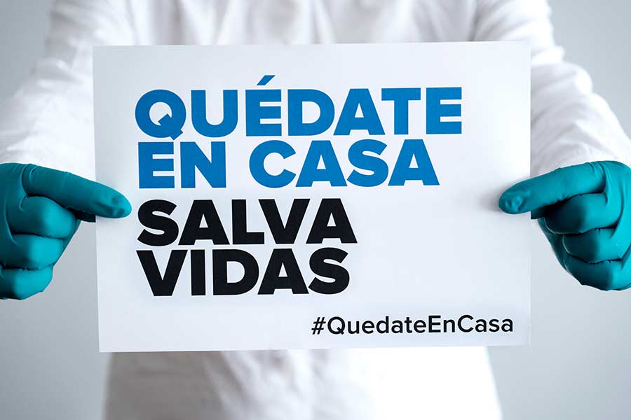 Manos sosteniendo un letrero con el mensaje: "Quédate en casa, salva vidas"