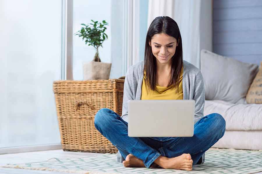 Joven feliz en su casa, sentada en el piso, utilizando su laptop