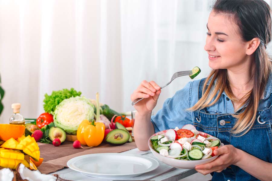 Mujer joven comiendo ensalda con gran variedad de vegetales