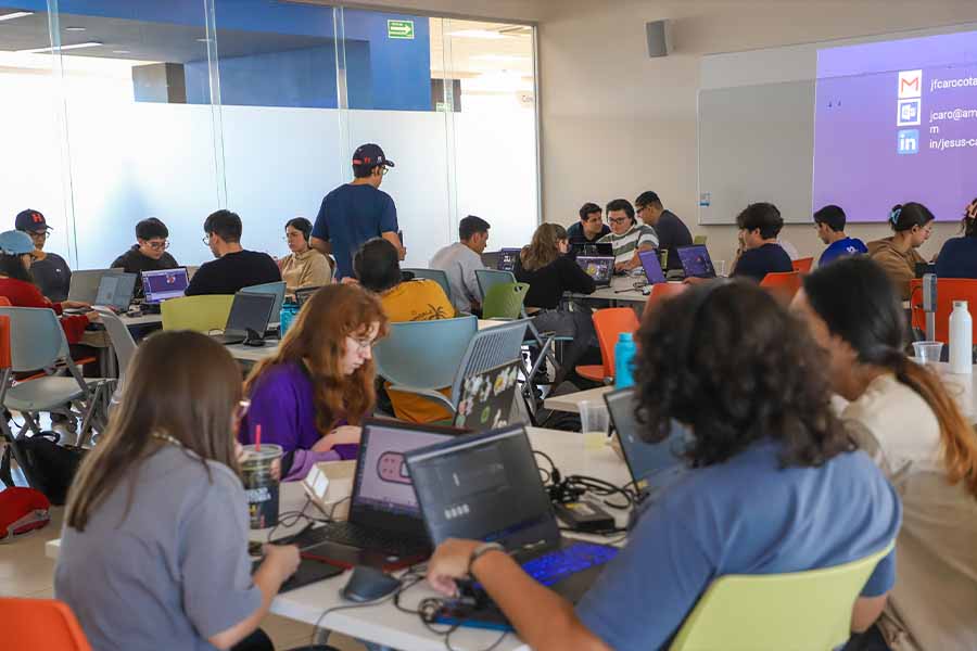 Salón lleno de estudiantes trabajando en sus computadoras. 