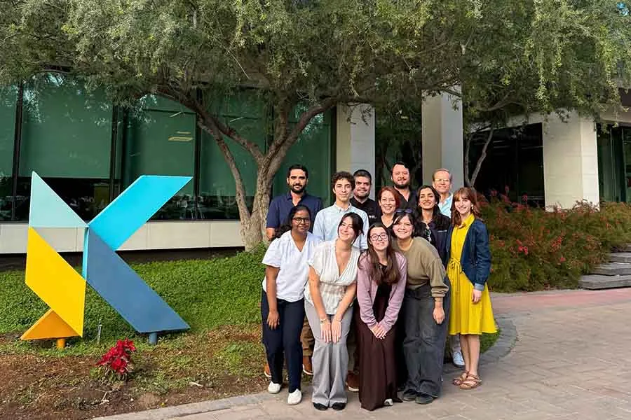 Grupo de 12 personas de g&eacute;neros y edades variadas, posando en grupo frente a un edificio.