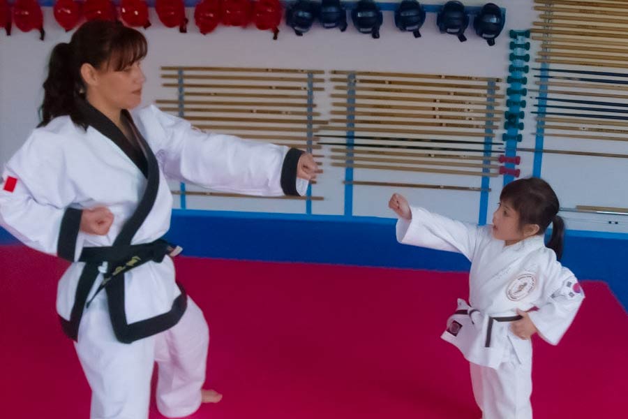 Sara Ramírez, entrenando Tang Soo Do con su instructora en un dojo, usando uniforme blanco con cinturón