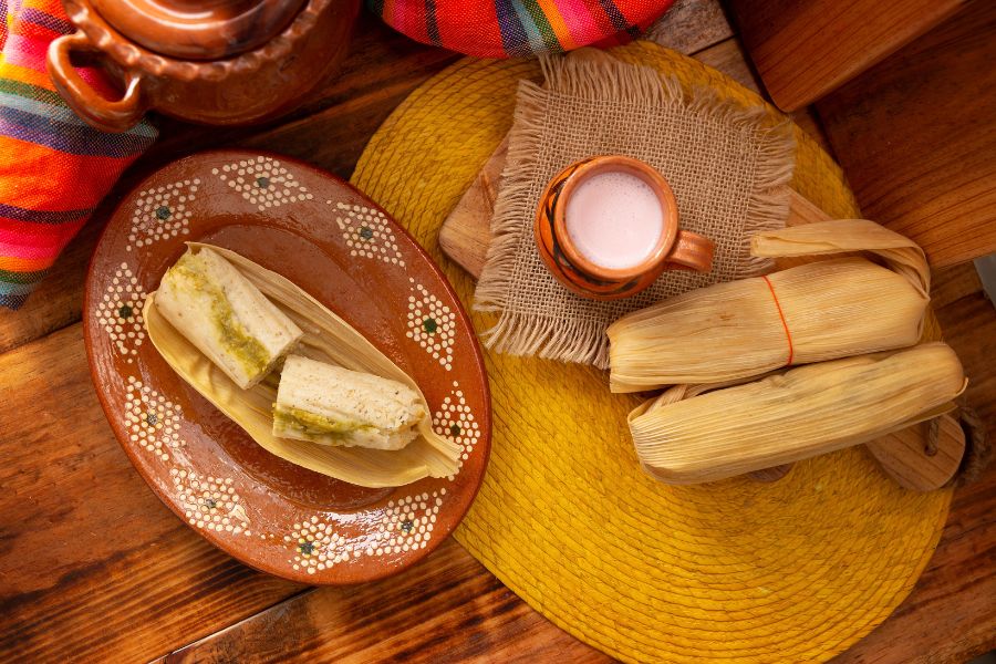 Tamales tradicionales mexicanos servidos en plato de barro, acompañados de atole, típicos de la cena de Navidad en México.