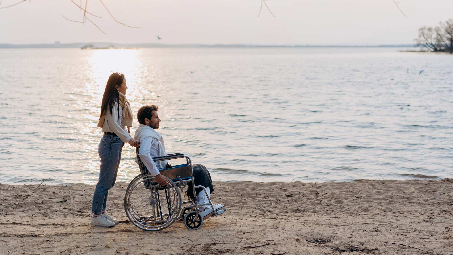 Hombre en silla de ruedas con su pareja en la playa viendo el atardecer