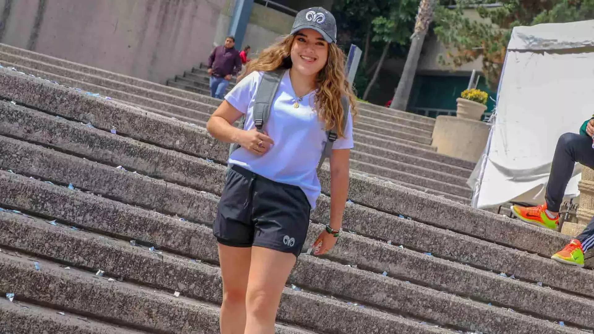 Chica modelando shorts y gorra gris con logo borregos