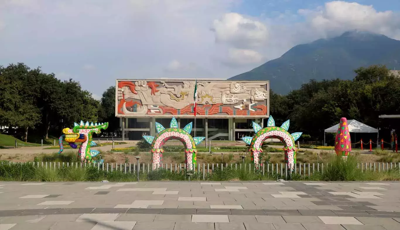 Un alebrije sobresale de entre la maleza frente al edificio de Rectoría