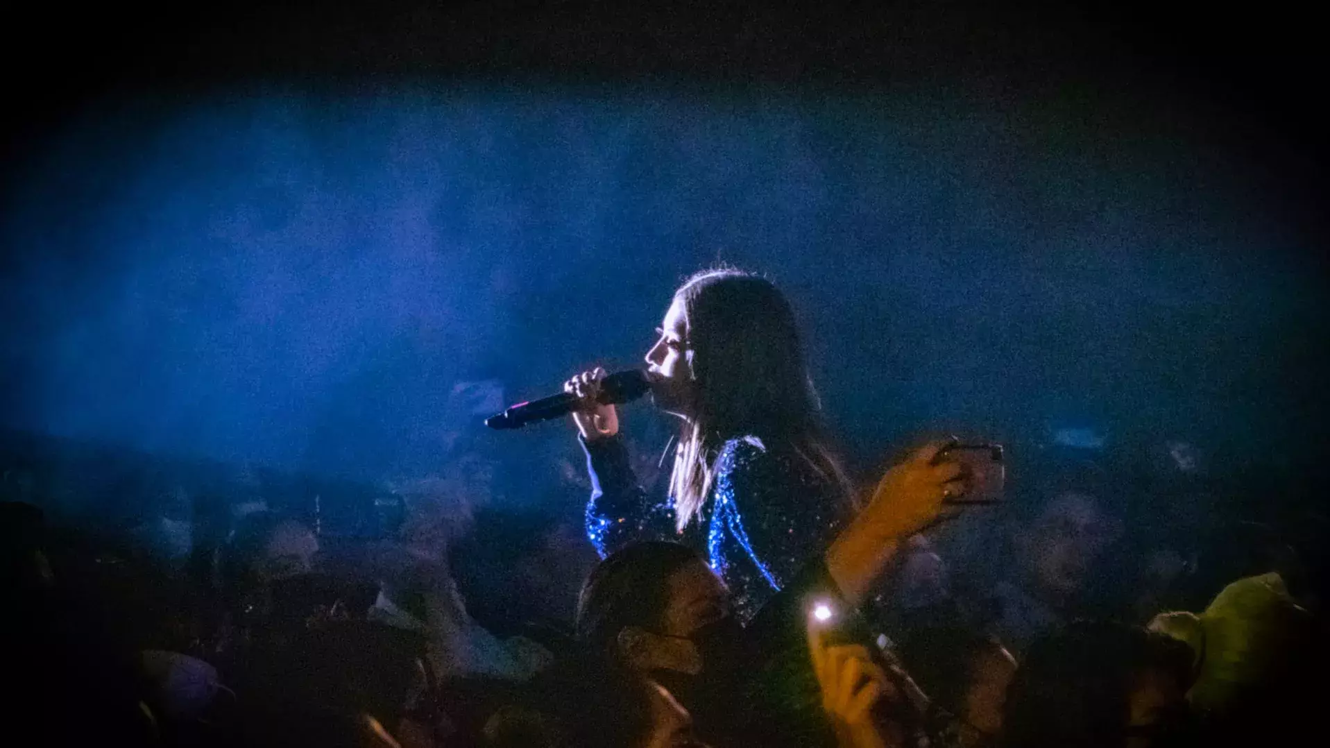 Alumna cantando con luz en cara en medio de la audiencia