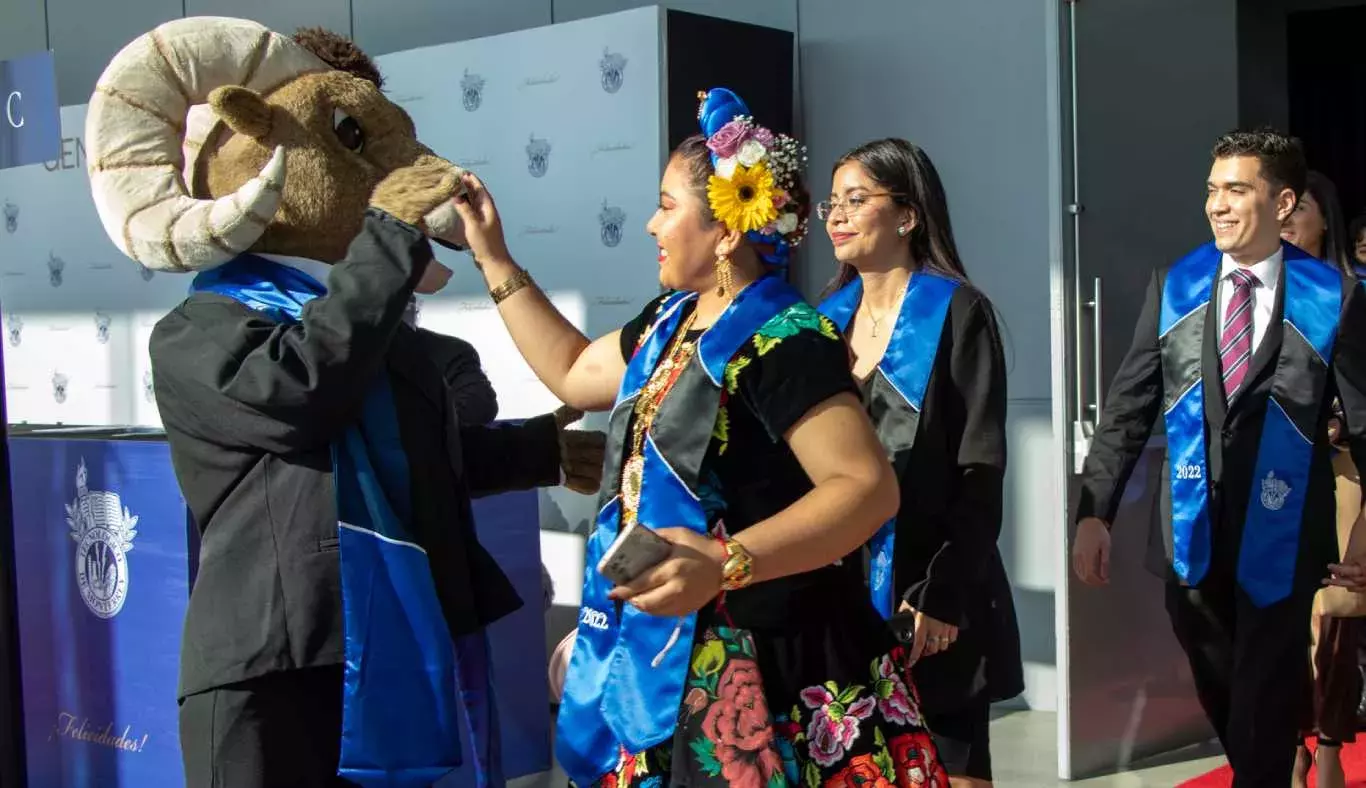 TEUS, la mascota del Tec, saludando a una egresada del campus Puebla con vestimenta típica del estado