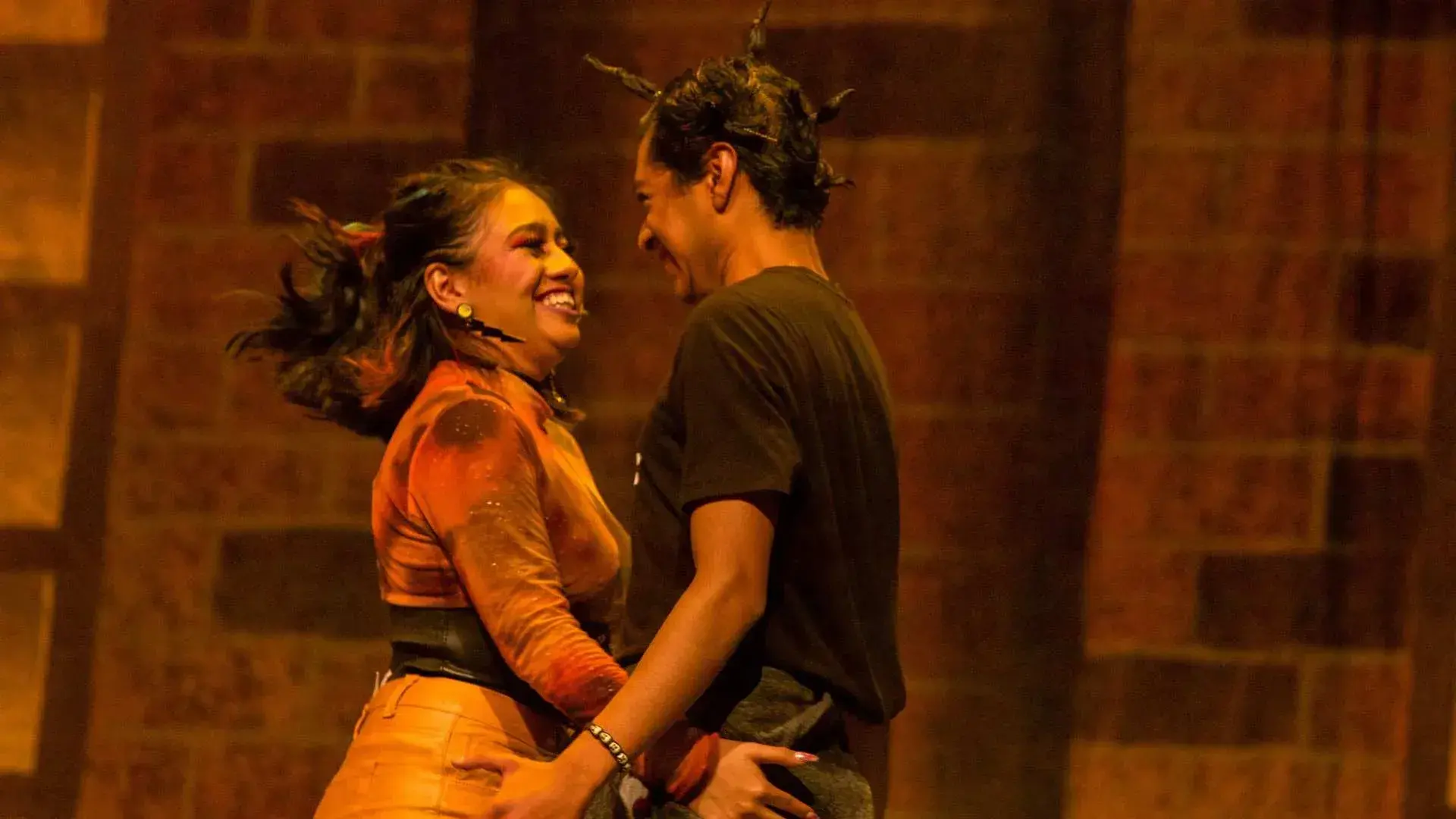 Alumnos sonríen mirándose mutuamente mientras interpretan escena de amor en la obra 