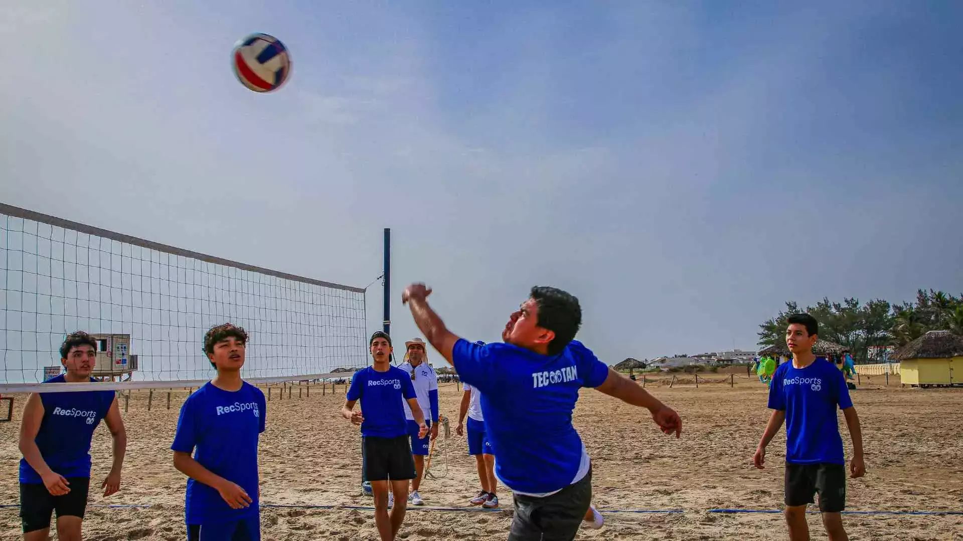 Alumnos jugando en equipo voleibol en la playa