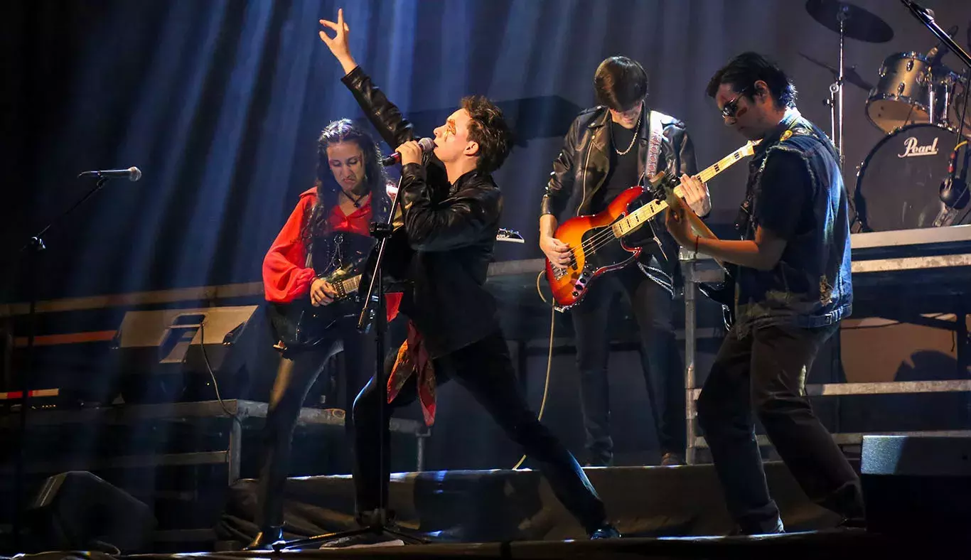 Cantante en pose de rock con tres guitarristas en el fondo.