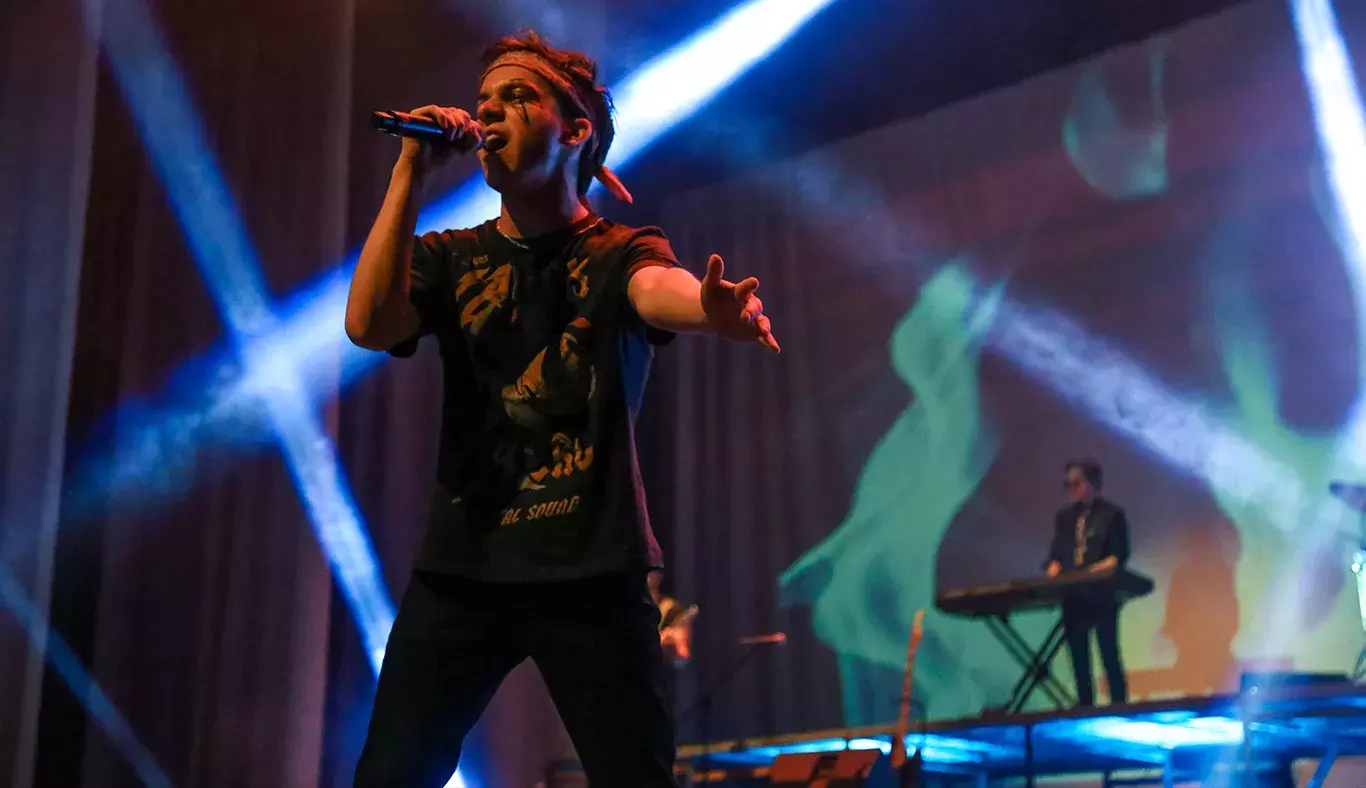 Cantante volteado hacia la izquierda con luces en el fondo. 