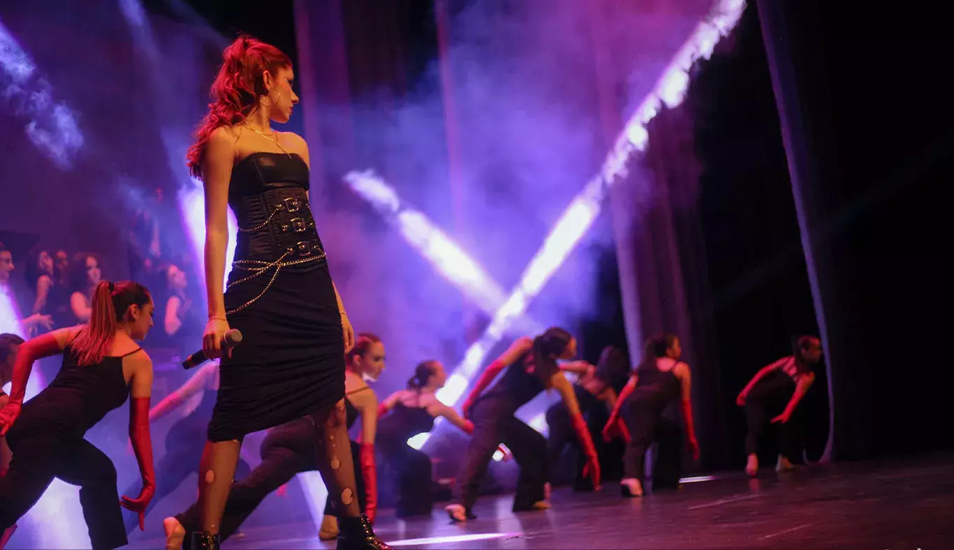 Cantante volteada hacia la izquierda con bailarinas de fondo. 