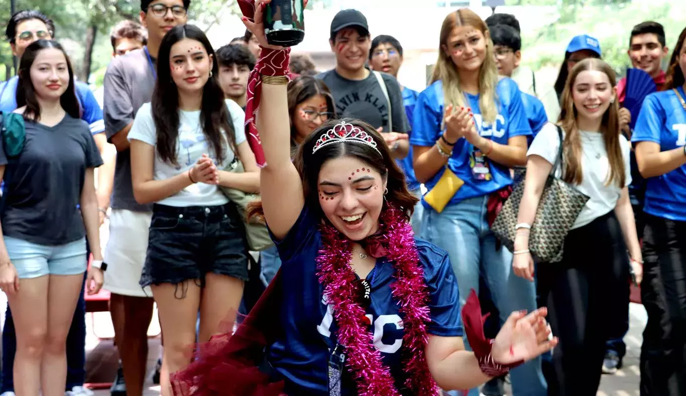 Alumna baila mientras alumnas y alumnos celebran.