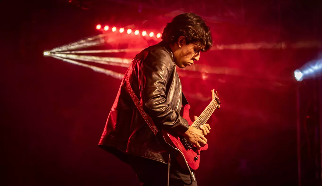 Andrés, guitarrista, en el escenario de Tec's Got Talent en el campus Hidalgo, concentrado en su interpretación con una guitarra eléctrica bajo luces rojas.