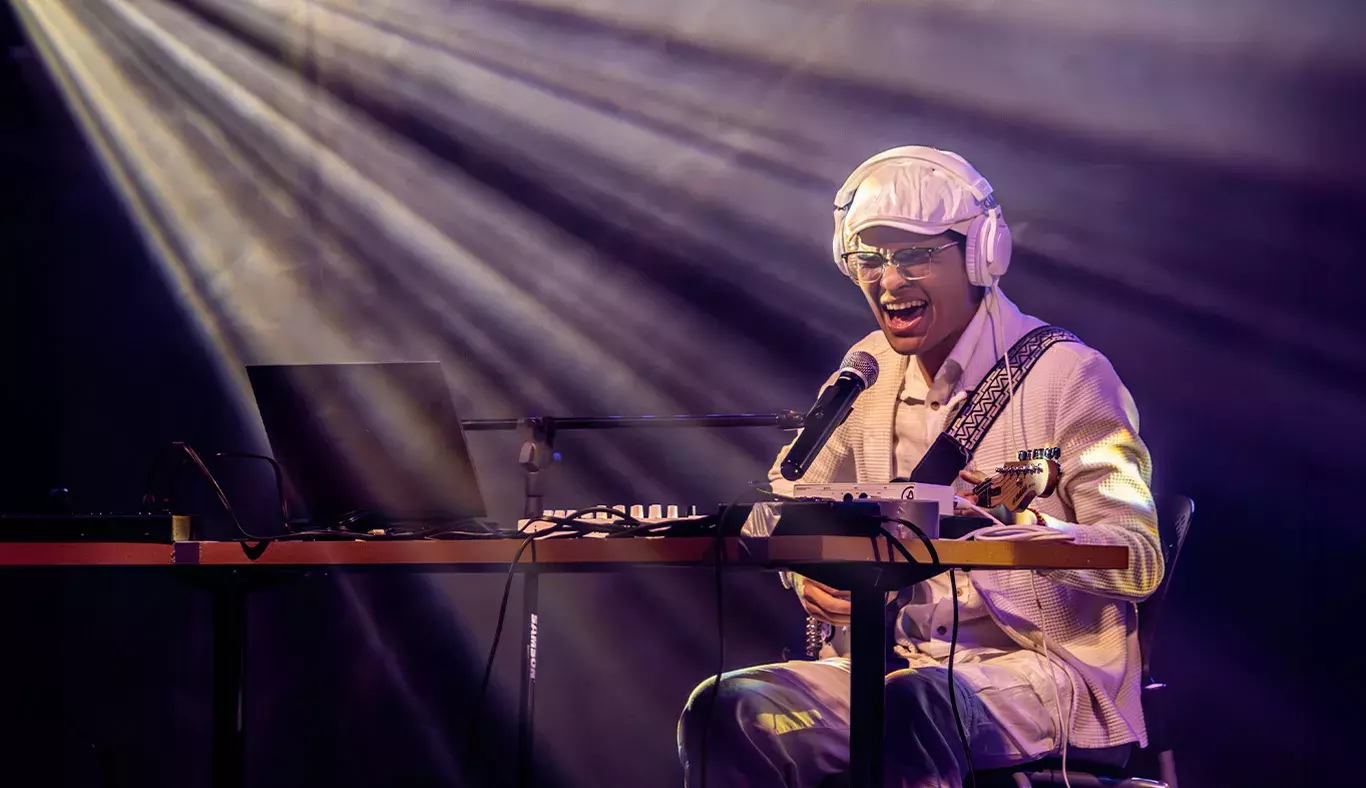 Jesús Alejandro, guitarrista y cantante, expresando emoción mientras canta en el escenario de Tec's Got Talent. Rodeado de su equipo de música, utiliza audífonos y micrófono, bajo los haces de luz.