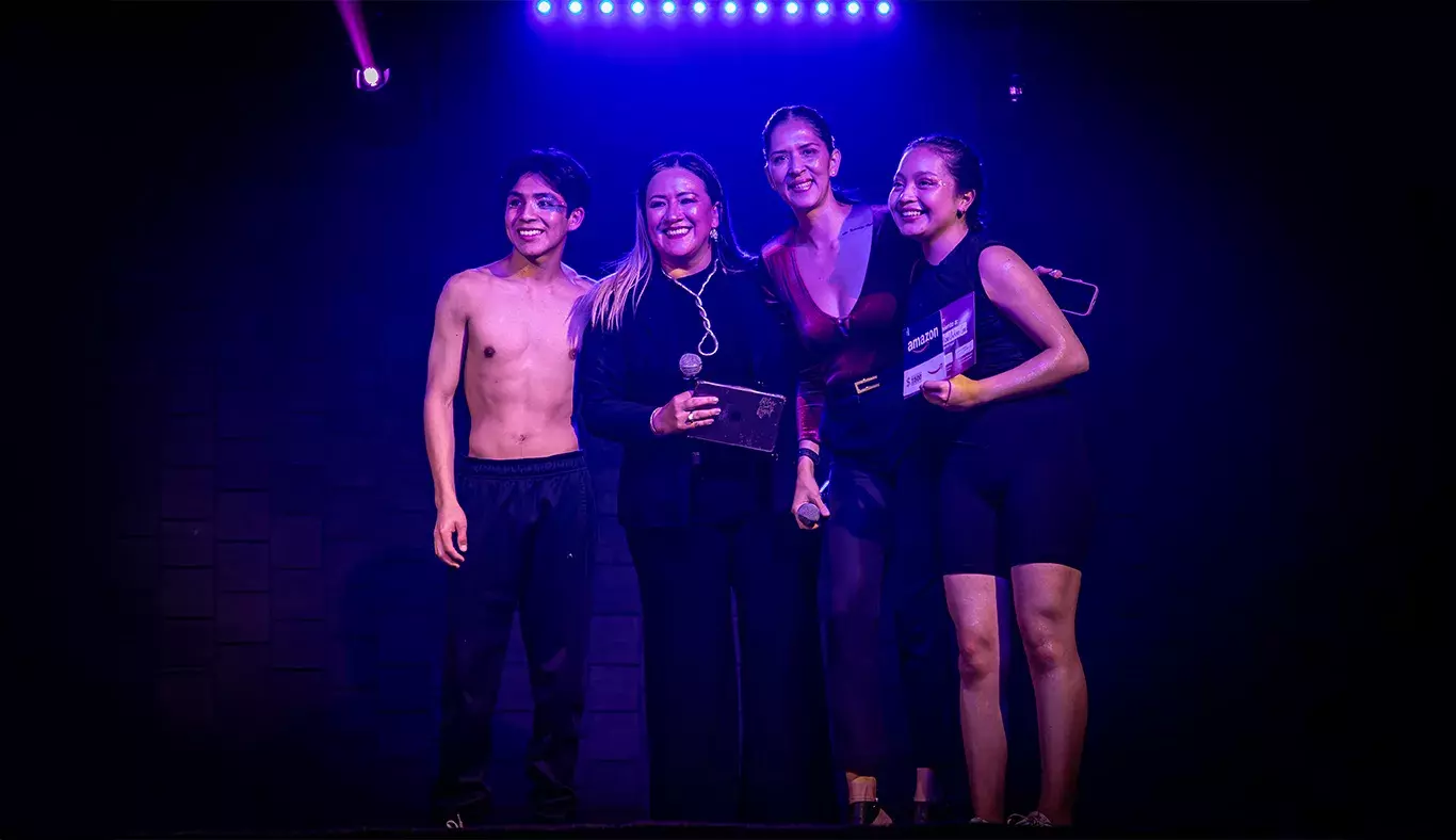 Nallely y Karol, ganadores del segundo lugar en Tec's Got Talent, posando junto a las mentoras de la comunidad KREI, sonriendo y sosteniendo su premio, bajo una iluminación azul.