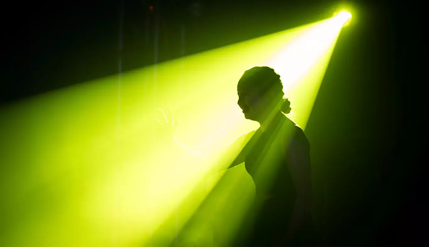 Nallely Ponce, actriz y bailarina, iluminada por un haz de luz verde en el escenario de Tec's Got Talent, creando una silueta.