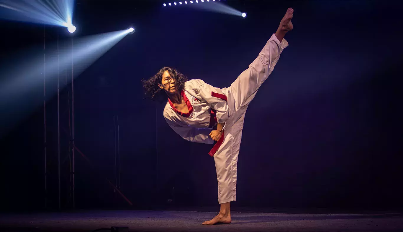 Rod Mendoza, karateka, ejecutando una patada alta con equilibrio durante su presentación en Tec's Got Talent en un escenario iluminado.