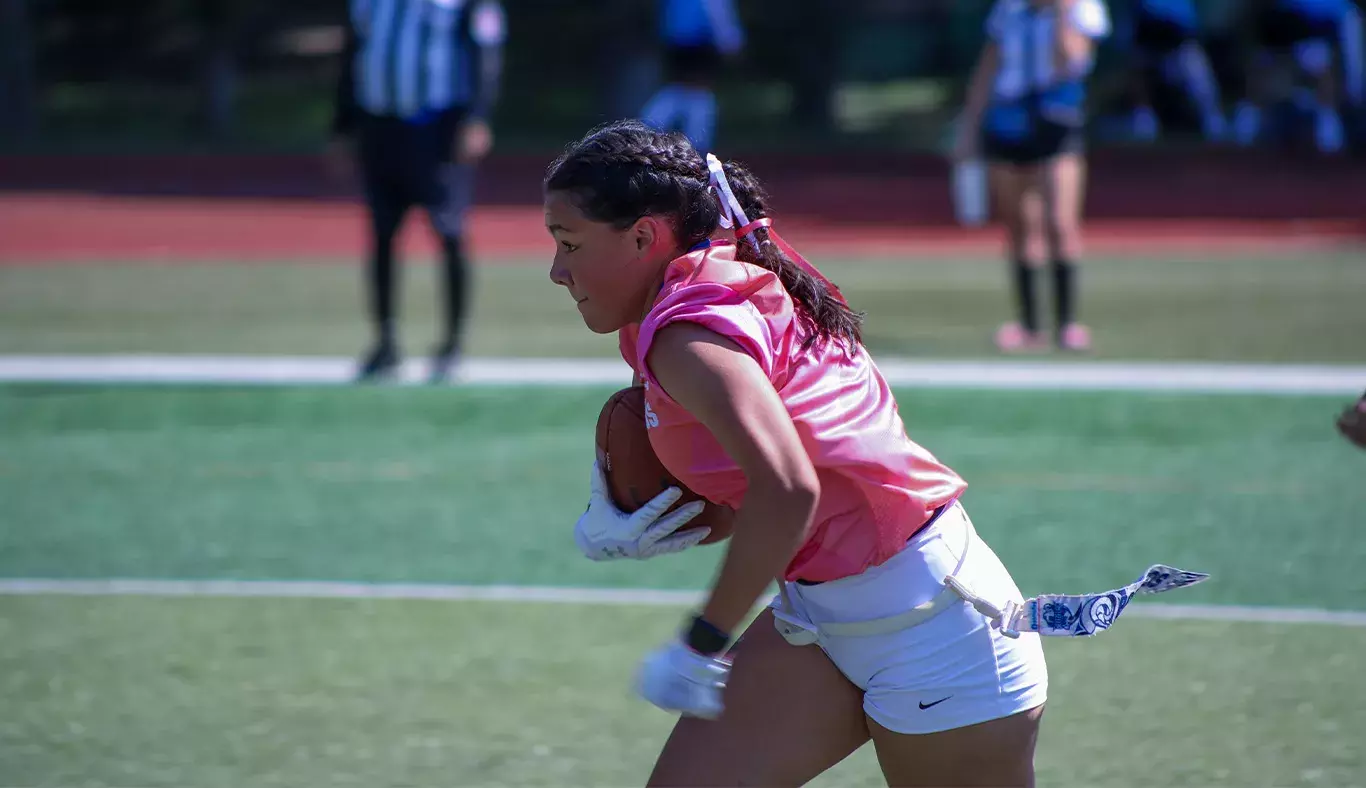 Chica corriendo con balon de futbol americano bajo el brazo. 