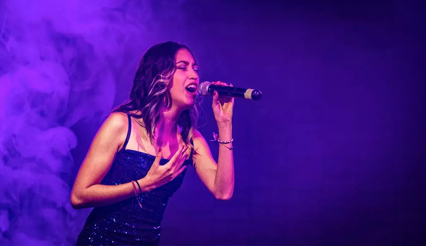 Valentina, cantante del representativo de campus Hidalgo, interpretando una canción en Tec's Got Talent, rodeada de una atmósfera púrpura y humo.