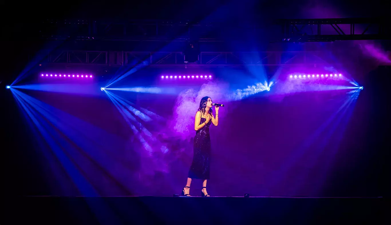 Valentina, estudiante de Estudios Creativos y cantante, interpretando en el escenario de Tec's Got Talent. Vestida de negro, rodeada de luces azules y púrpuras.