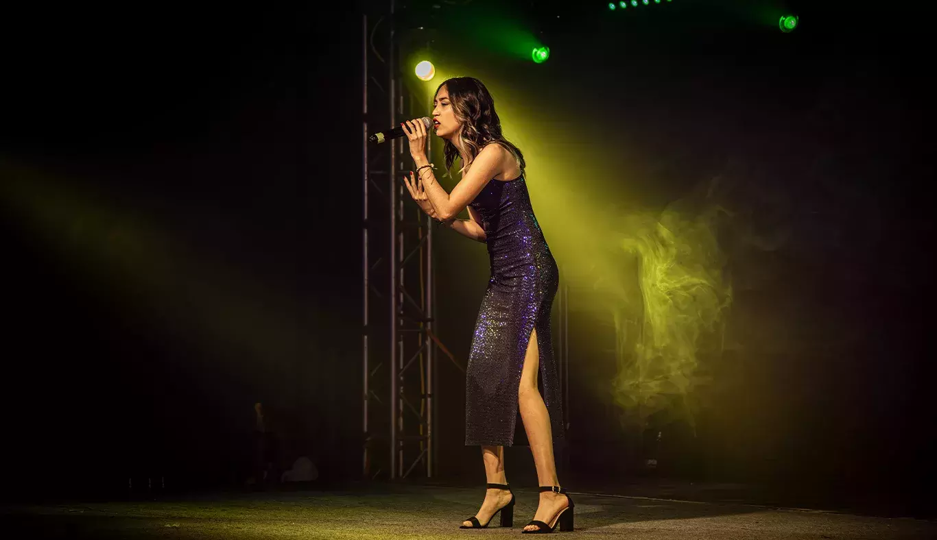 Valentina Fuentes, cantante del representativo de Arte y Cultura, interpretando una canción en el escenario con un vestido brillante y luces amarillas.