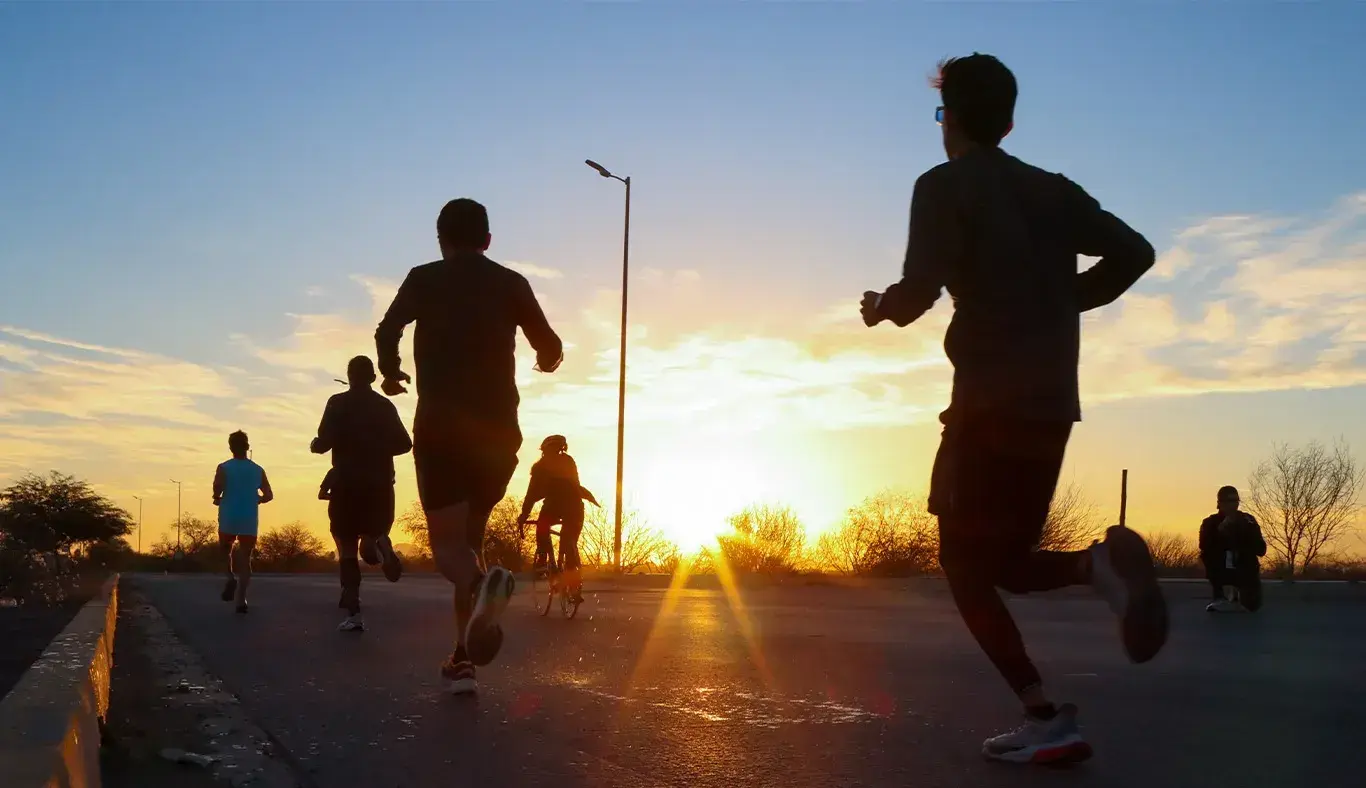 Personas corriendo a contraluz con amanecer de fondo