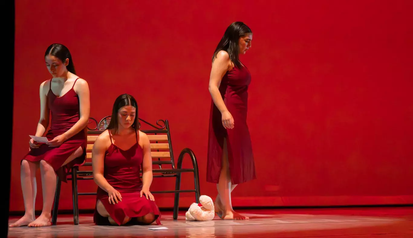 Tres bailarinas realizan formas sobre banco en un fondo rojo