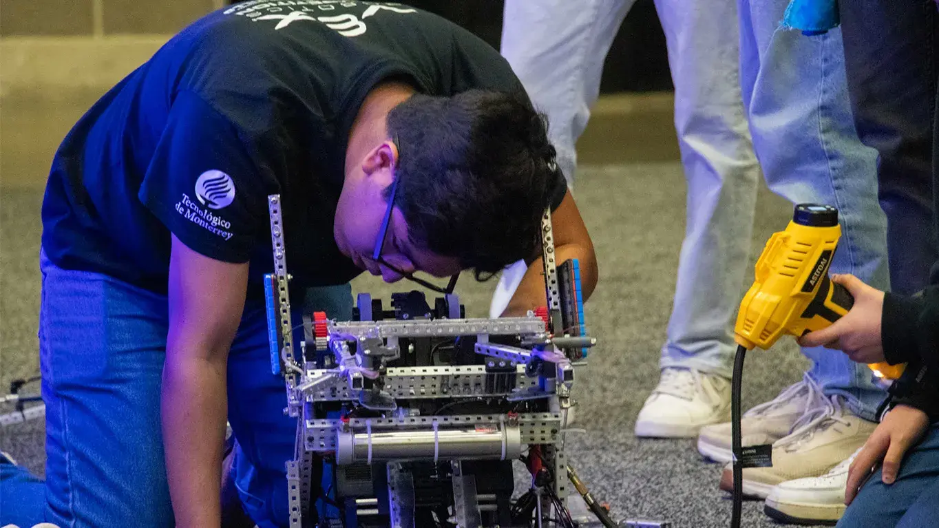 Alumno agachado reparando un robot.